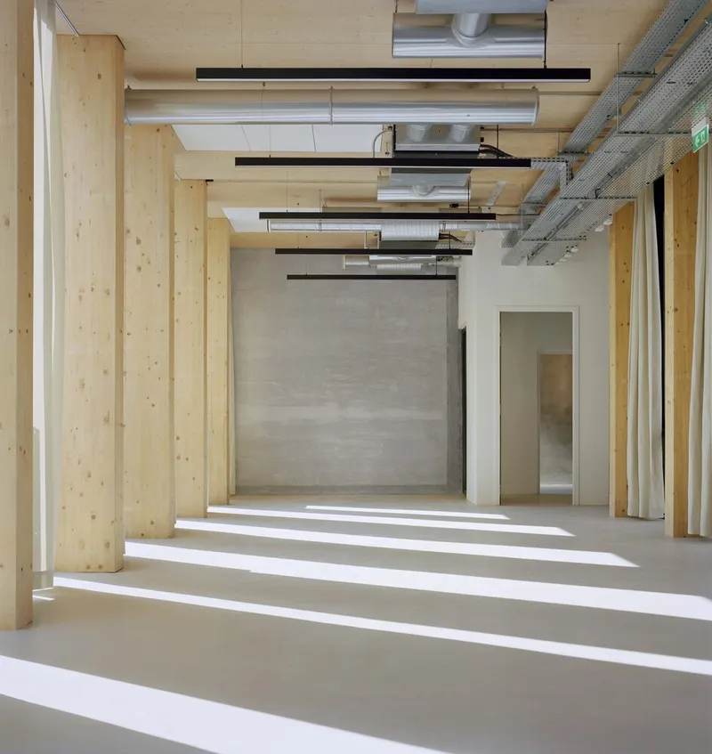 Light-filled corridor with exposed laminated timber columns and rectangular beams creating rhythmic shadows on the polished concrete floor