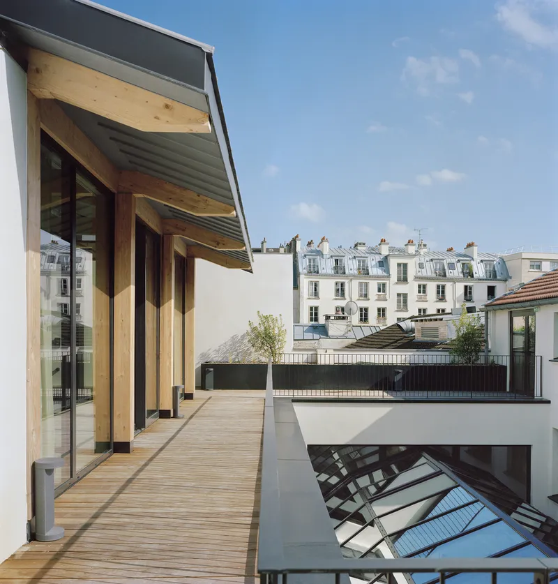 Rooftop terrace with timber decking and angled overhang framing a skylight opening under afternoon sky