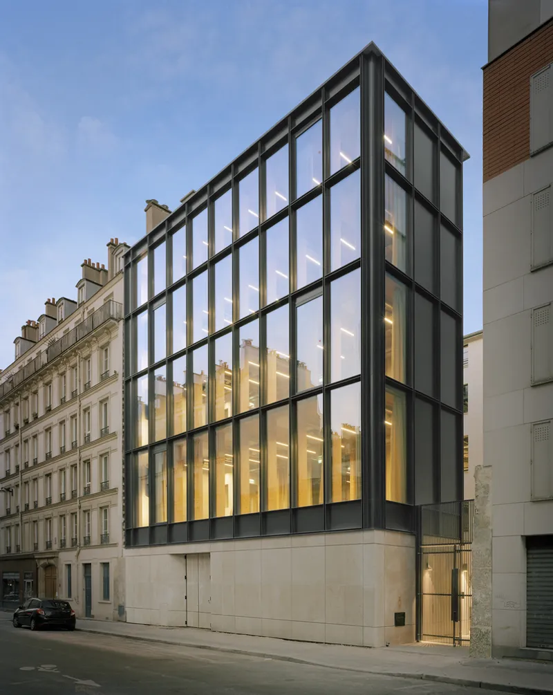 Street facade with gridded black steel frame and glazing above a solid concrete base at dusk