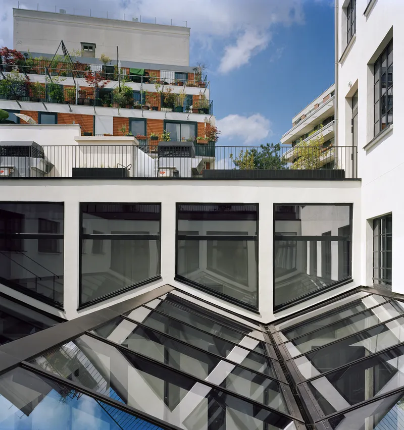 Courtyard view showing projecting white-framed windows above angled glass skylights with planted terrace beyond