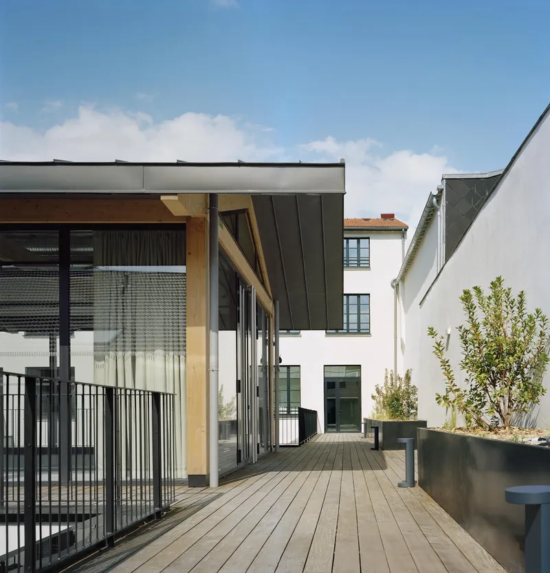 Timber-decked rooftop terrace with metal railing and dark metal-clad pavilion under blue sky