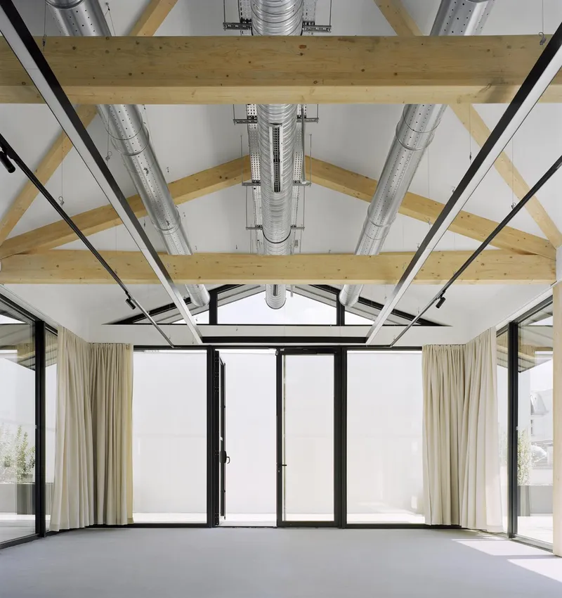 Vaulted ceiling with exposed timber trusses and metal ductwork above glazed doors opening to a terrace