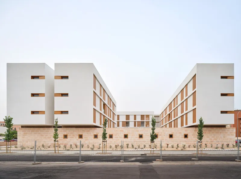 Street view of white residential blocks with timber framed windows above a stone base with planted trees