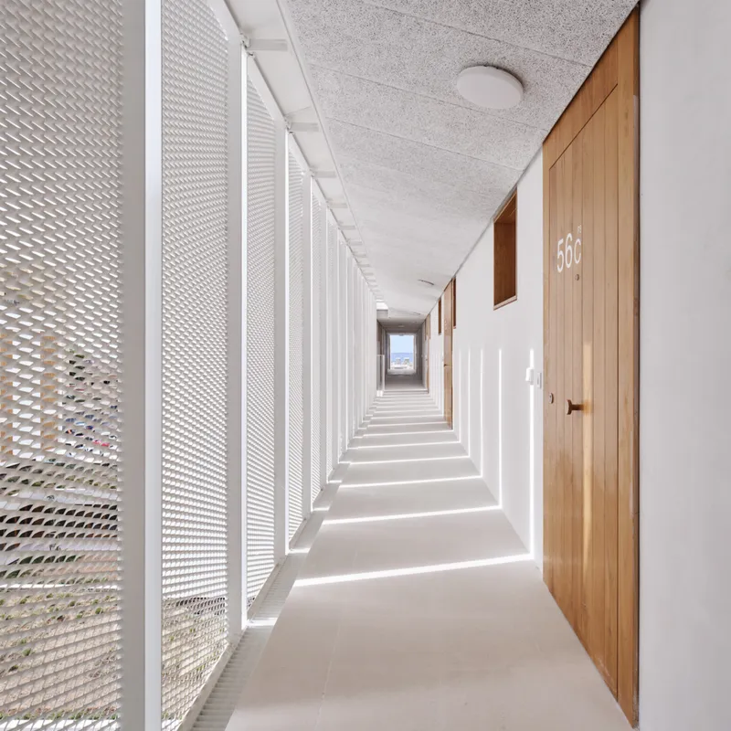 Corridor with perforated metal screen wall casting rhythmic shadows on white walls and timber doors