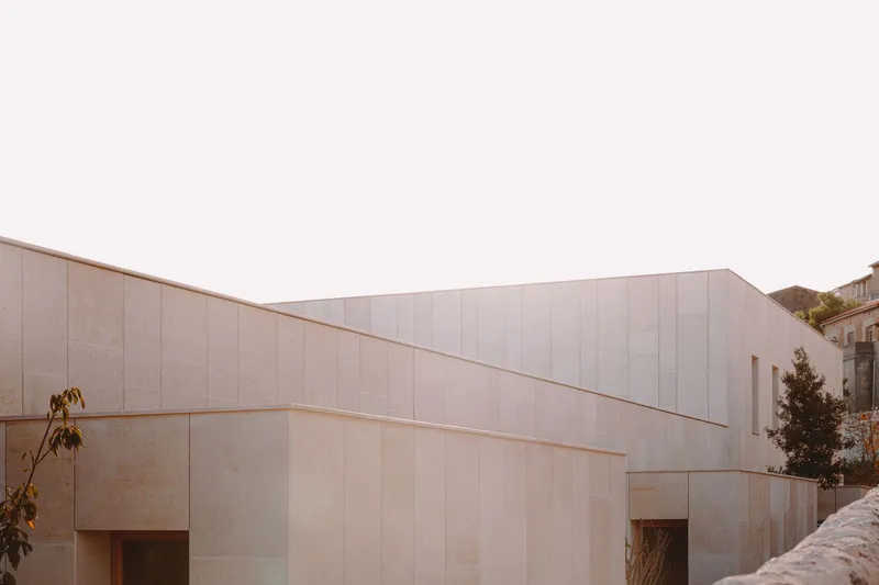 Street view of the angled stone panel facade with recessed entry openings at dusk