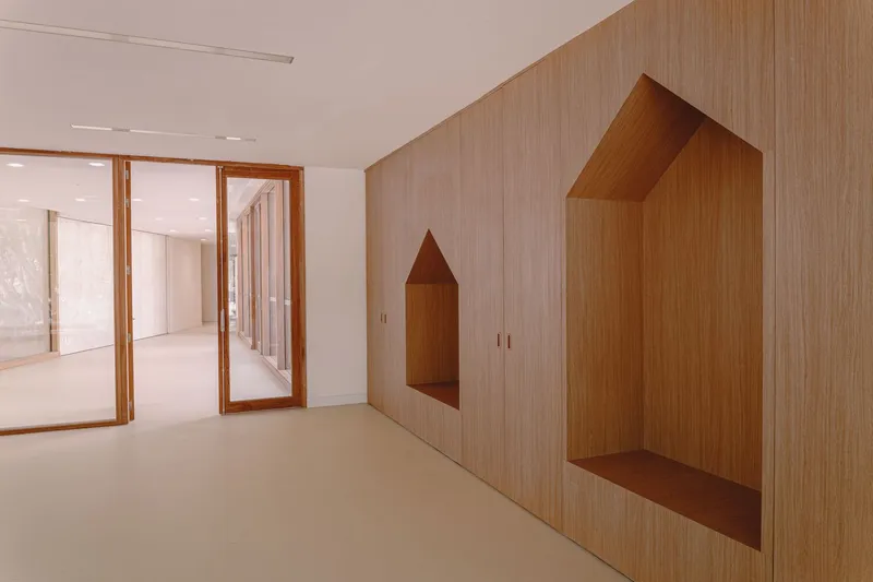 Interior wall with light wood paneling featuring house-shaped recessed niches beside timber-framed glass doors