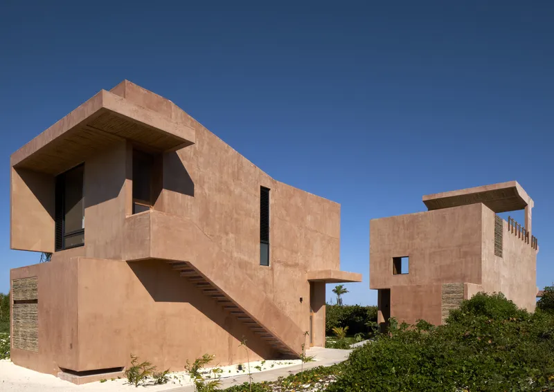 Two rammed earth volumes with exterior staircase and white gravel landscaping under clear blue sky