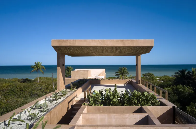 Rooftop garden with planted beds and pergola structure framing ocean views and palm trees