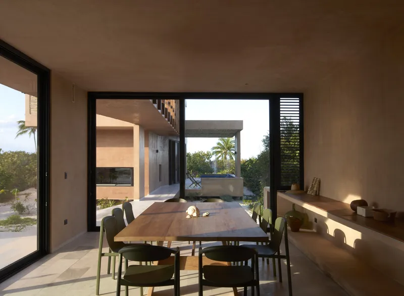 Dining room with live-edge wood table looking through glazed openings to courtyard and pergola