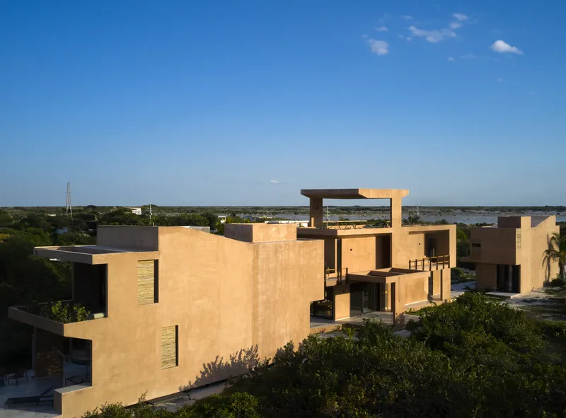 Aerial view of clustered rammed earth volumes with rooftop terraces overlooking flat coastal landscape