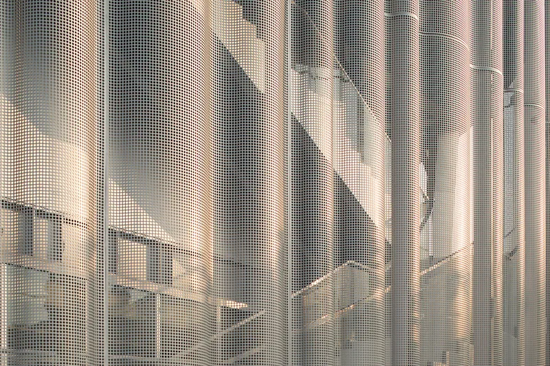 Close-up of perforated metal screen showing pixelated shadow patterns cast by afternoon sunlight