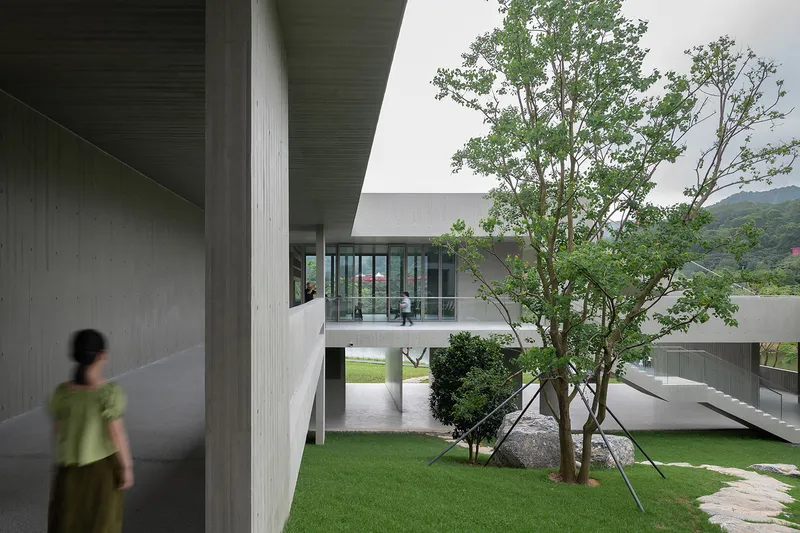 Interior courtyard with planted lawn and trees framed by concrete columns and bridges on an overcast day