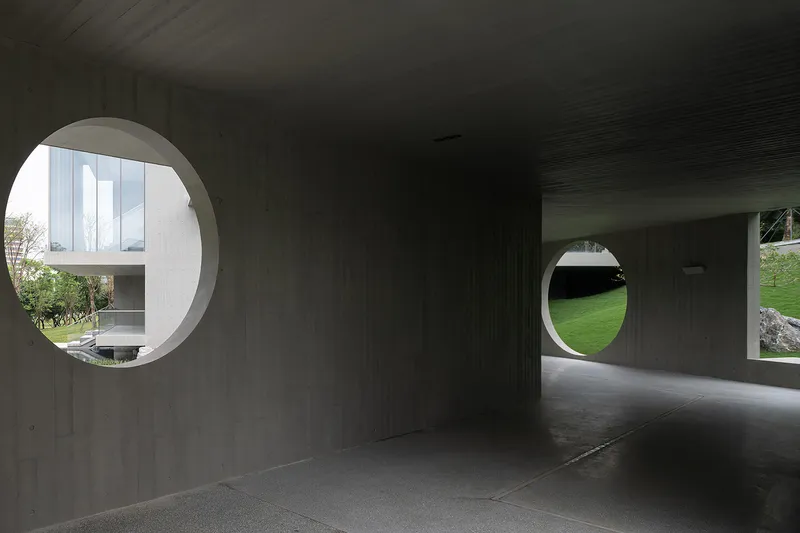 Concrete corridor with ribbed ceiling and circular apertures framing views of a grassy slope beyond