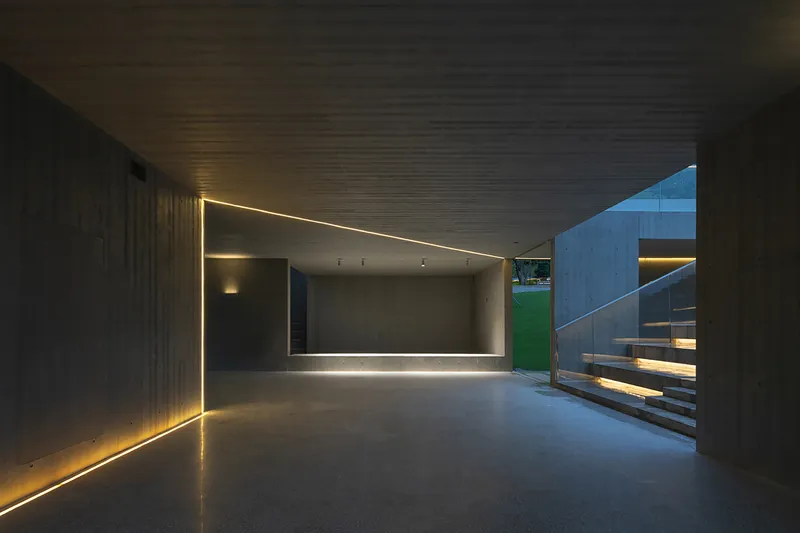 Interior passage with linear LED light strips embedded in concrete walls and ribbed ceiling at dusk