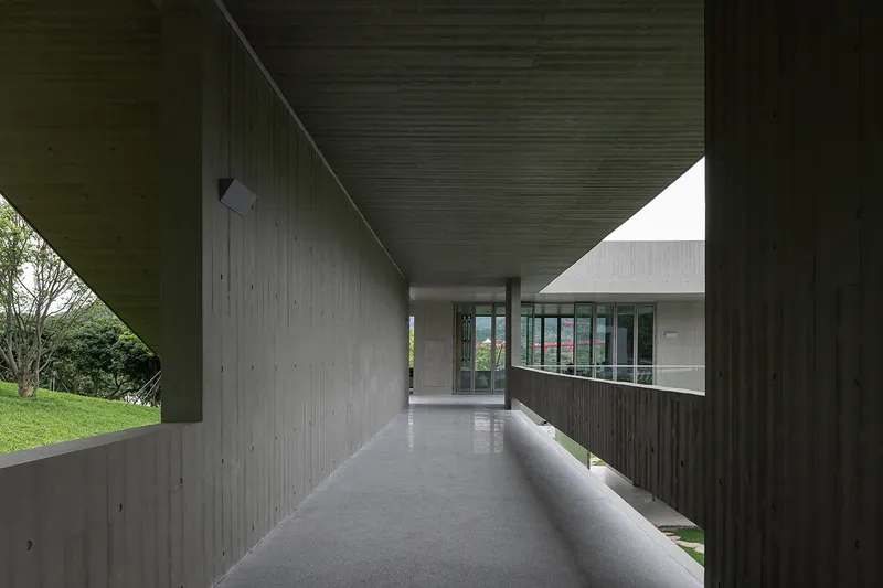 Concrete corridor with board-formed walls and glazed end wall overlooking green lawn and trees
