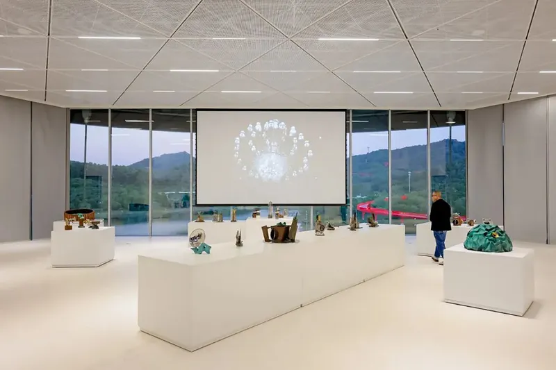 Gallery space with white display plinths and sculptural objects beneath geometric perforated ceiling panels