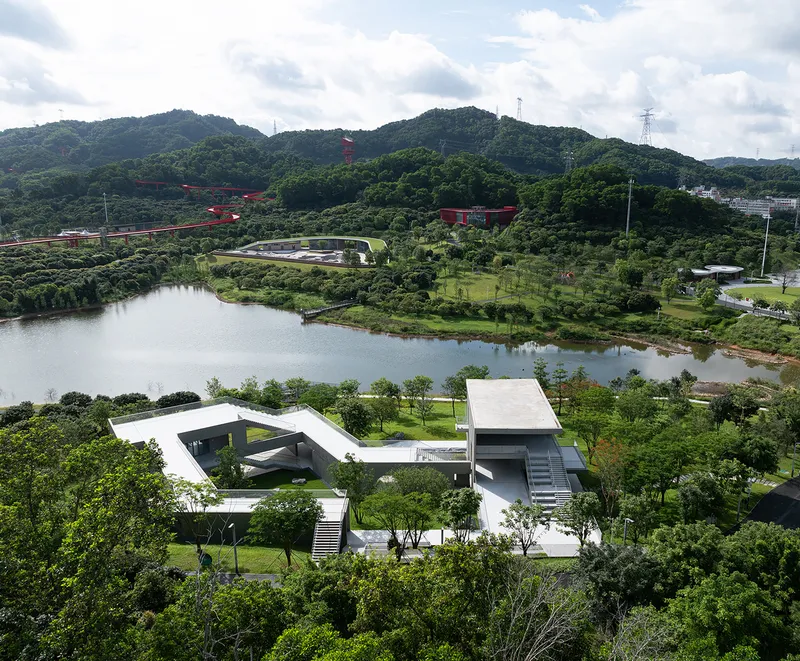 Elevated view of the flat roofed buildings in parkland beside a pond with forested hills