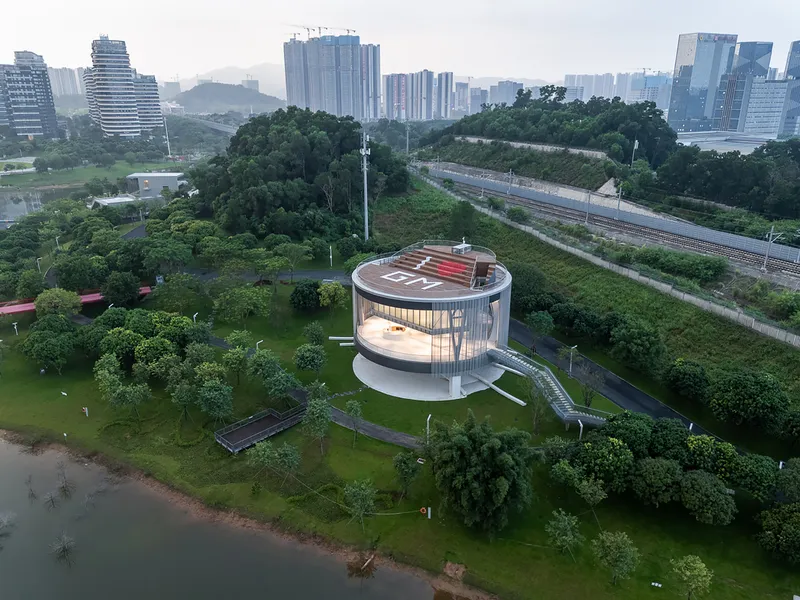 Circular pavilion with translucent vertical screen facade and red rooftop helipad at dusk