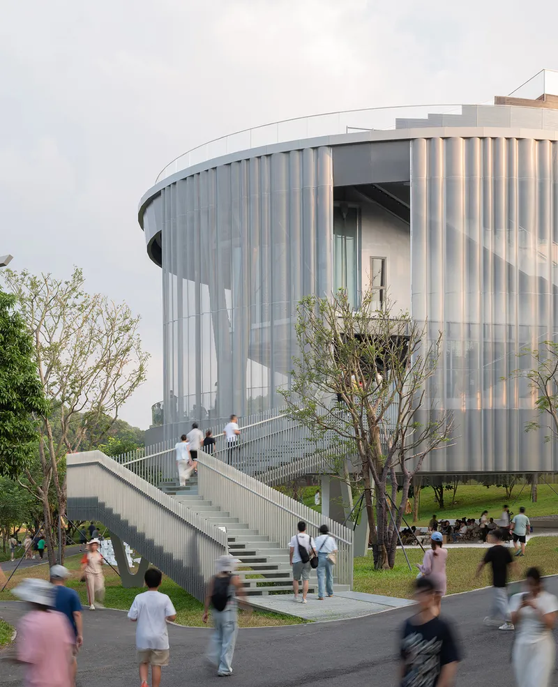 Curved facade with vertical glass louvers and exterior staircase with blurred visitors ascending