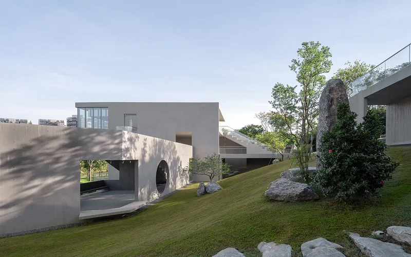 Concrete volumes with circular and arched openings set in a landscaped garden with grass and boulders