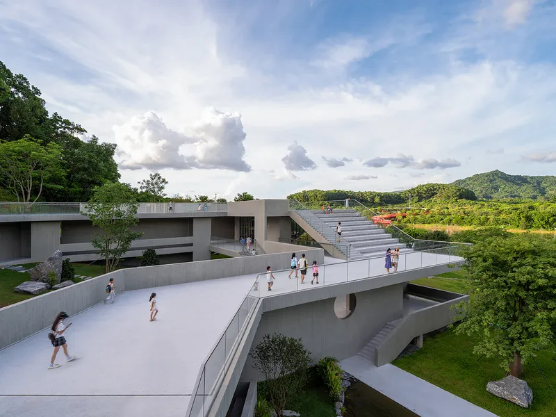 Ramped concrete plaza with visitors walking beneath a cloudy sky and distant green hills