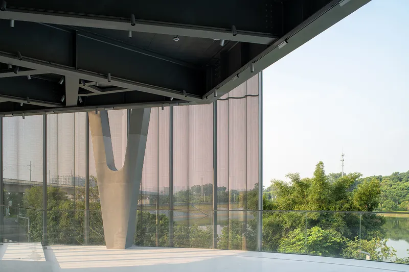 Floor-to-ceiling glass wall with translucent curtains overlooking trees and a lake in soft light