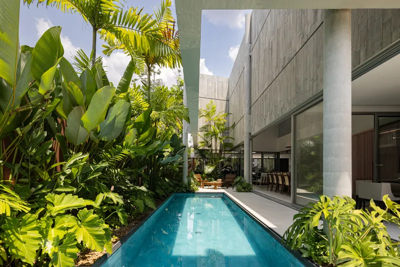 Narrow lap pool flanked by board-formed concrete walls and dense tropical plantings under afternoon sun