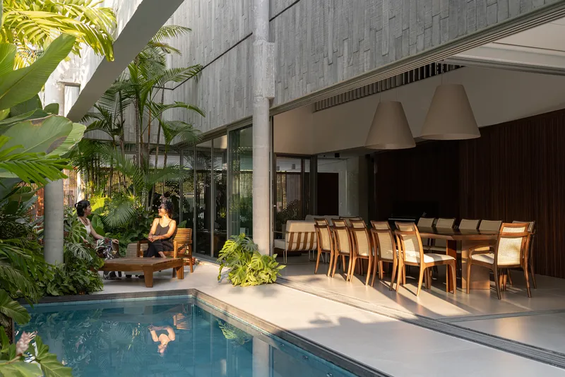 Poolside terrace with timber dining table and concrete pendant lights at dusk with seated figures