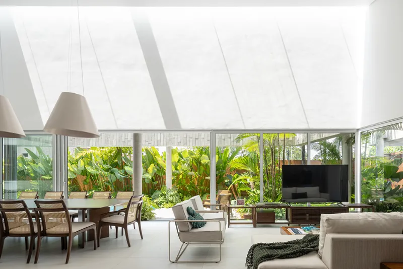 Open living and dining space with sloped skylight casting linear shadows above floor-to-ceiling garden windows