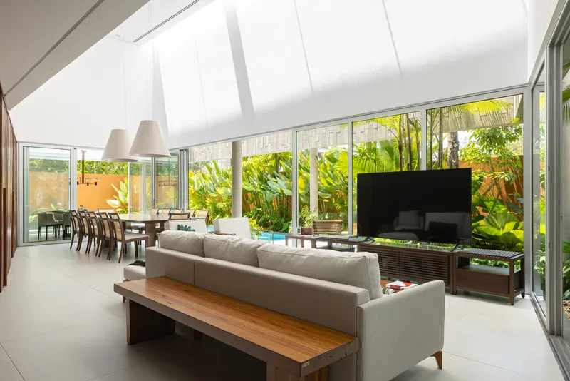 Open-plan living and dining space with floor-to-ceiling glass walls overlooking a planted courtyard with palms