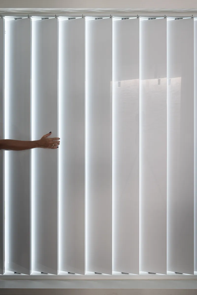 Vertical louver blinds with hand pulling one panel to adjust interior daylight