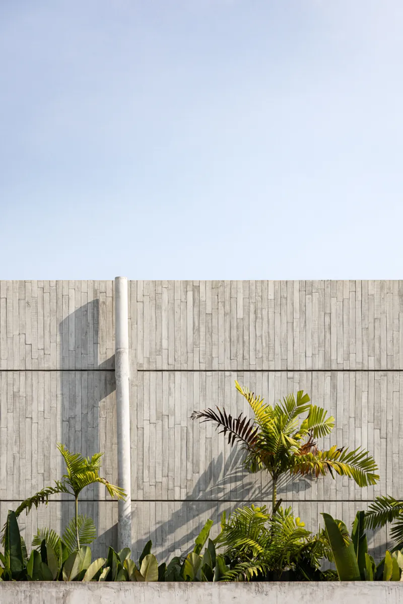 Exterior facade with staggered tile cladding and concrete base planted with palms casting afternoon shadows