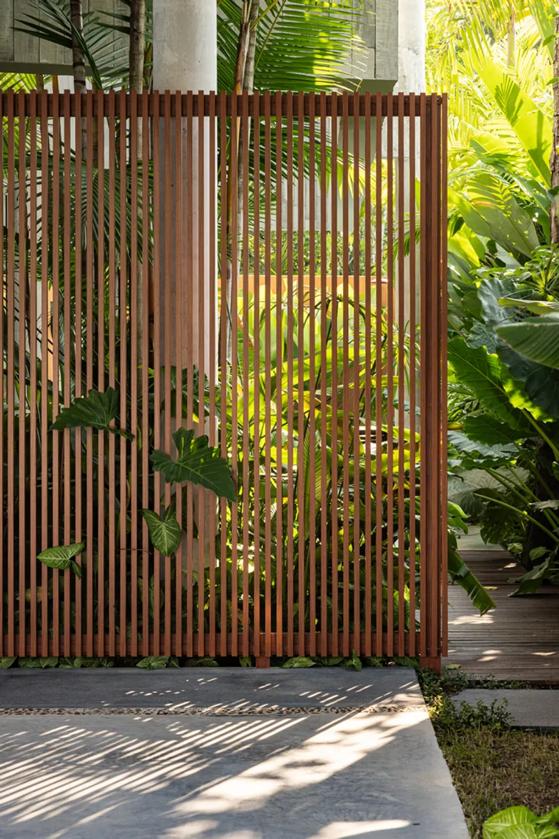 Vertical timber slat screen filtering sunlight among tropical plantings in a courtyard