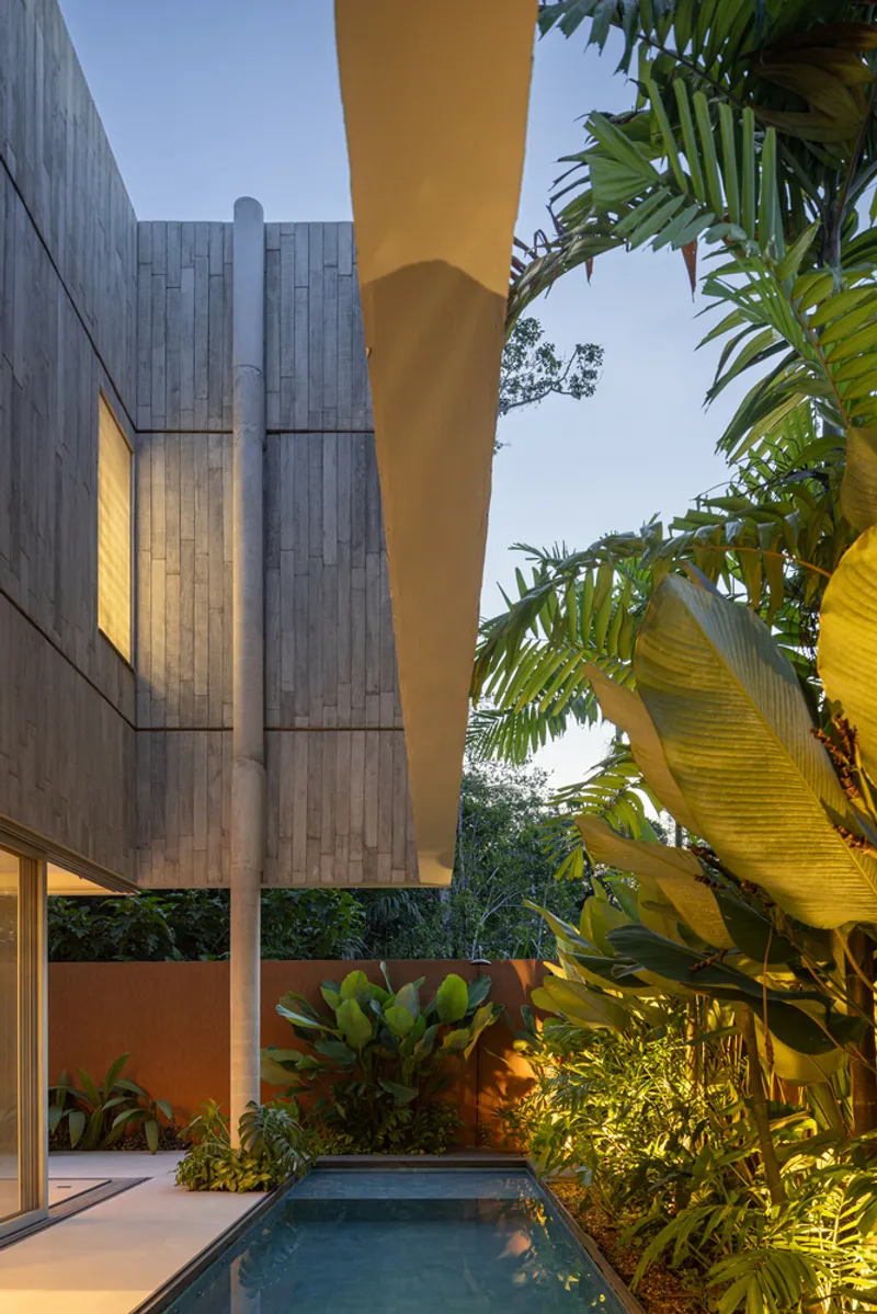 Courtyard pool framed by cantilevered yellow soffit and concrete pillar amid tropical plantings at dusk