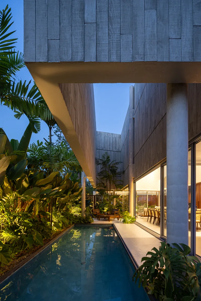 Narrow lap pool between concrete columns under elevated timber-clad volume at twilight