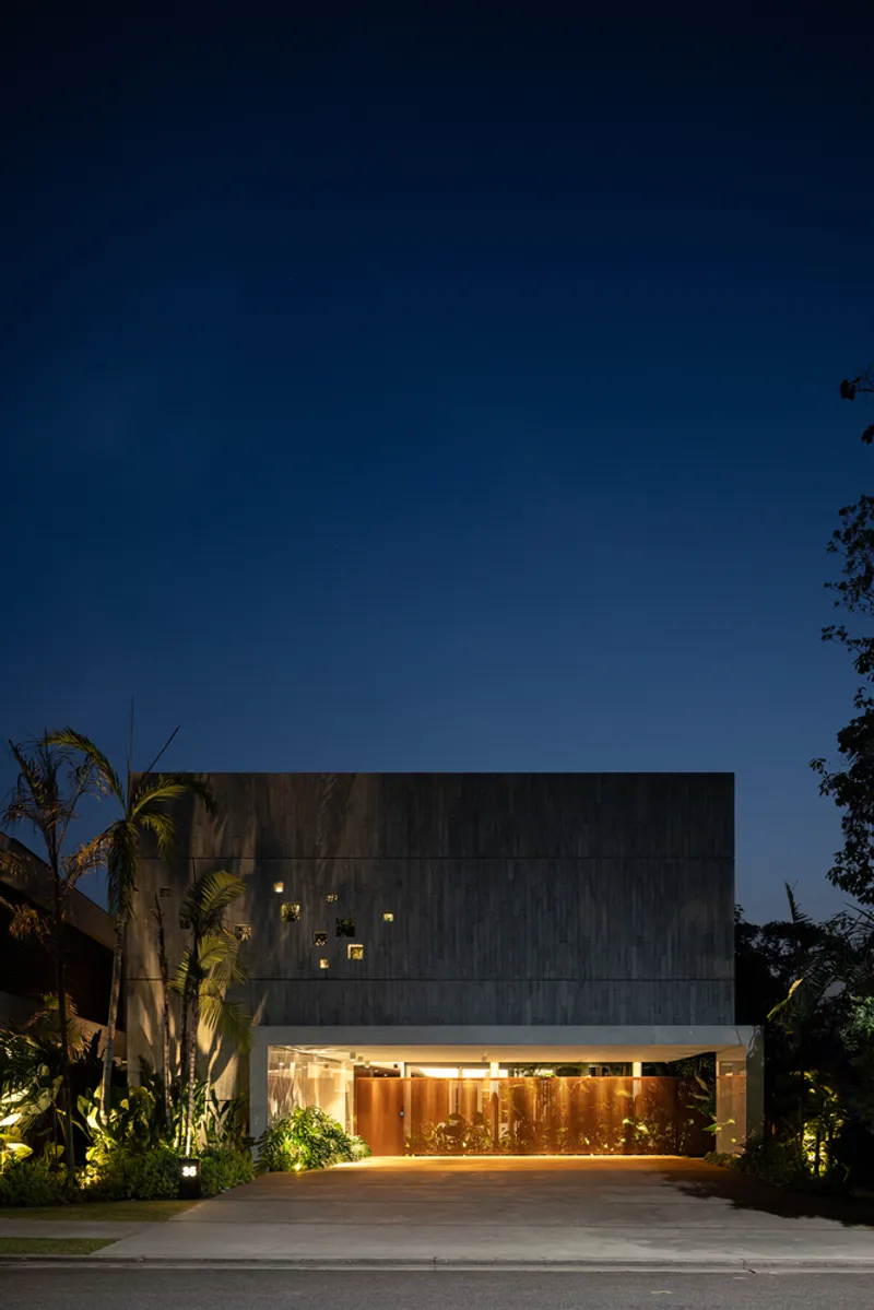 Street facade with vertical timber cladding above illuminated ground floor and palm trees at night