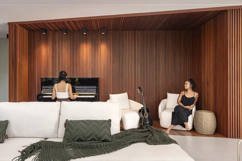 Living room with vertical timber slat wall alcove housing a piano and two seated figures