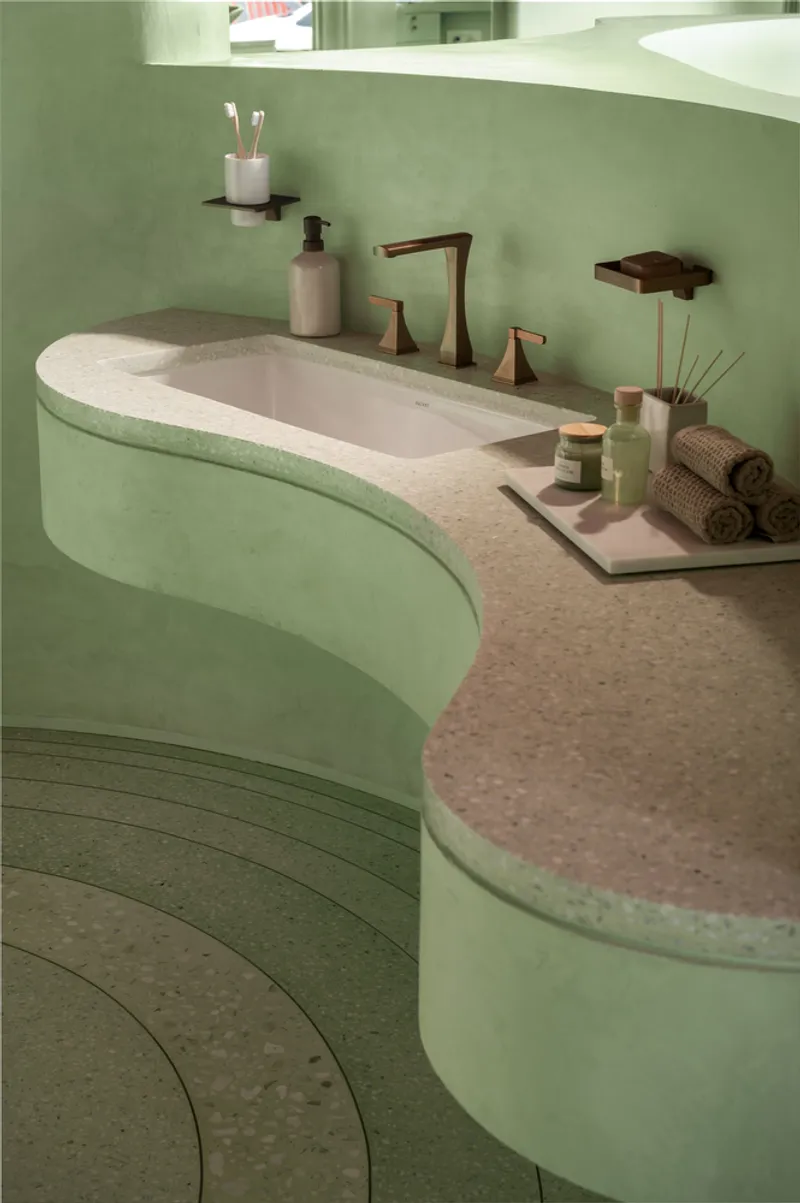 Curved vanity with integrated sink and terrazzo countertop against soft green plaster walls