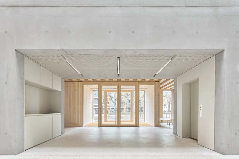 Entry lobby with concrete walls and timber-framed glass doors leading to a courtyard beyond