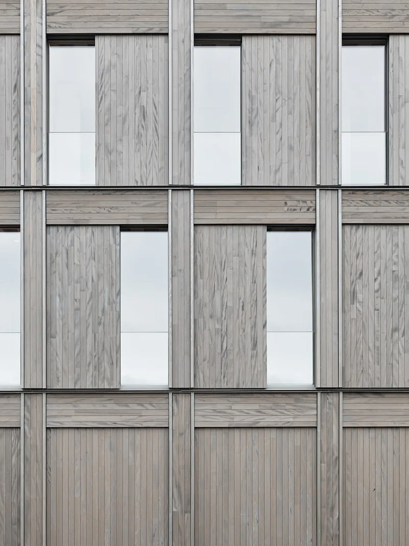 Close-up of the facade grid showing alternating timber panels and recessed glazing with slim frames