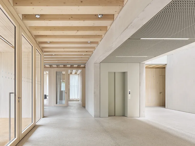 Interior corridor with exposed timber ceiling beams and elevator framed by perforated metal ceiling panels