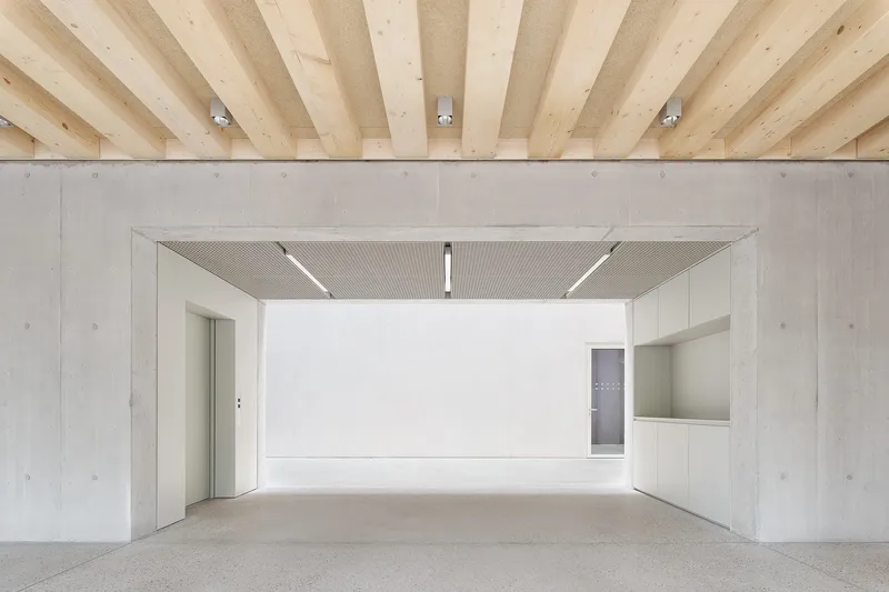 View through concrete portal into white-walled space with perforated ceiling soffit and recessed lighting