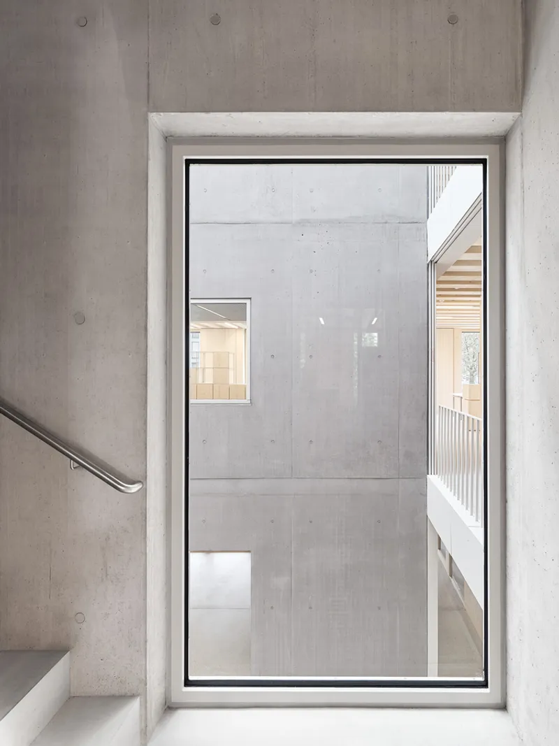 Floor-to-ceiling window in concrete stairwell overlooking the interior atrium and adjacent timber balcony
