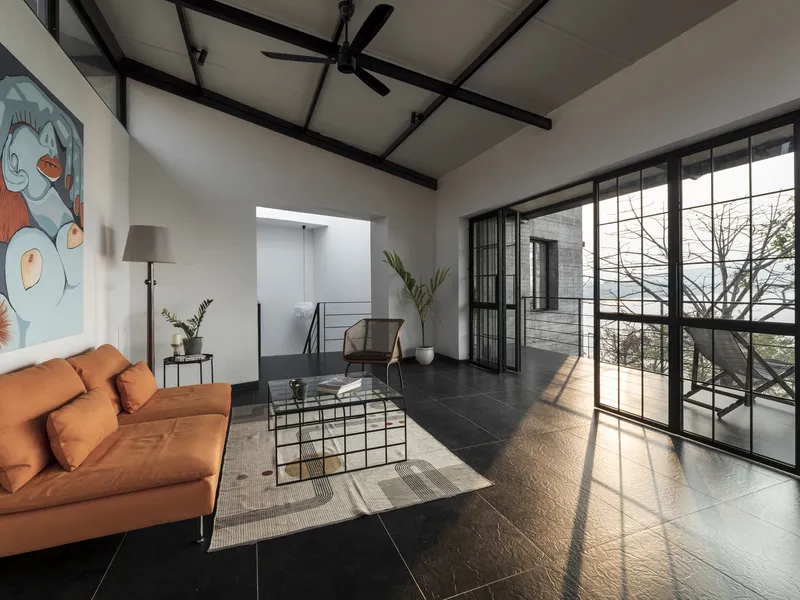 Living room with exposed black steel beams and floor-to-ceiling gridded glazing framing bare branches outside
