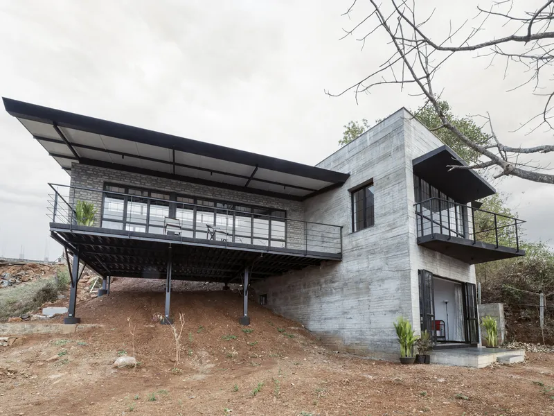 Board-formed concrete facade with cantilevered steel canopy and glazed openings under overcast sky