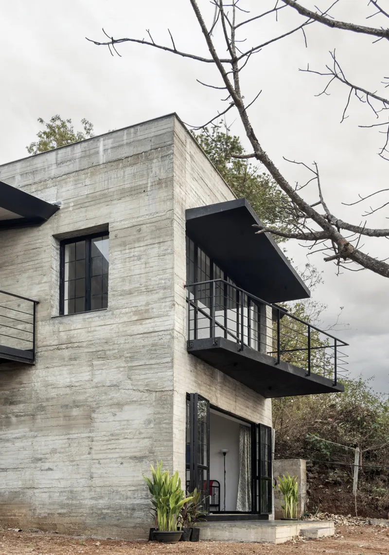 Corner of the concrete tower with cantilevered steel balcony and bare tree branch in foreground