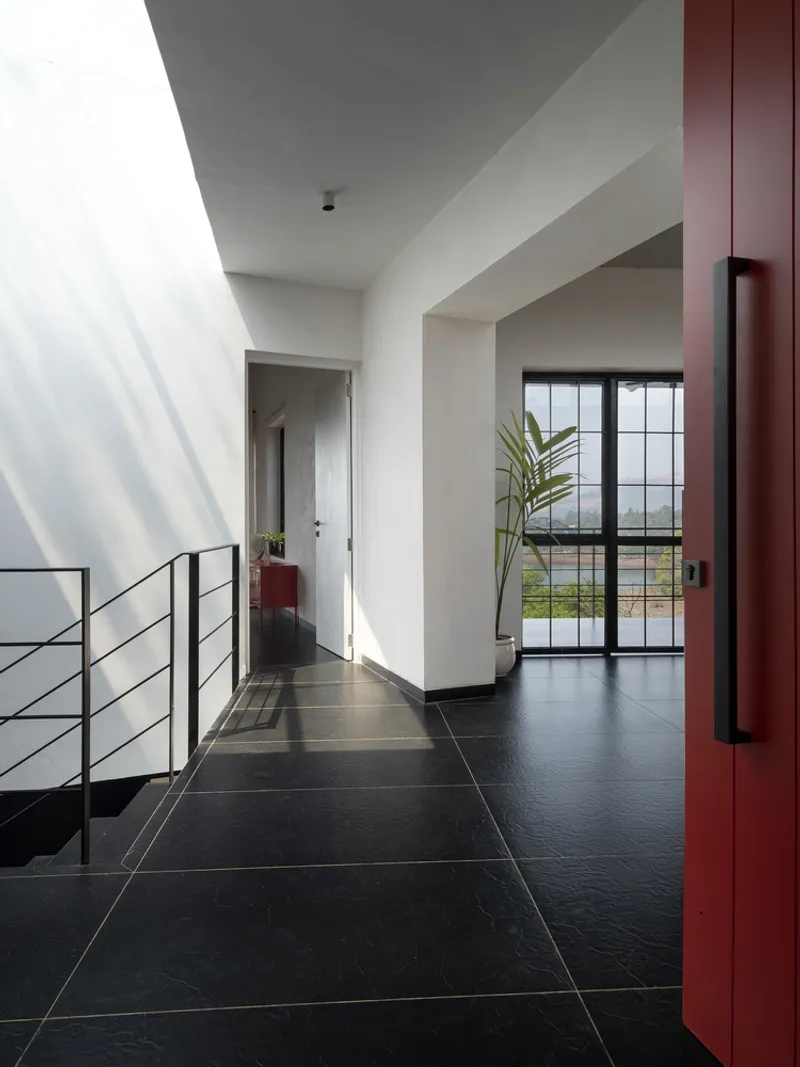 Upper corridor with black tile floor, cable railing and red steel column in bright daylight