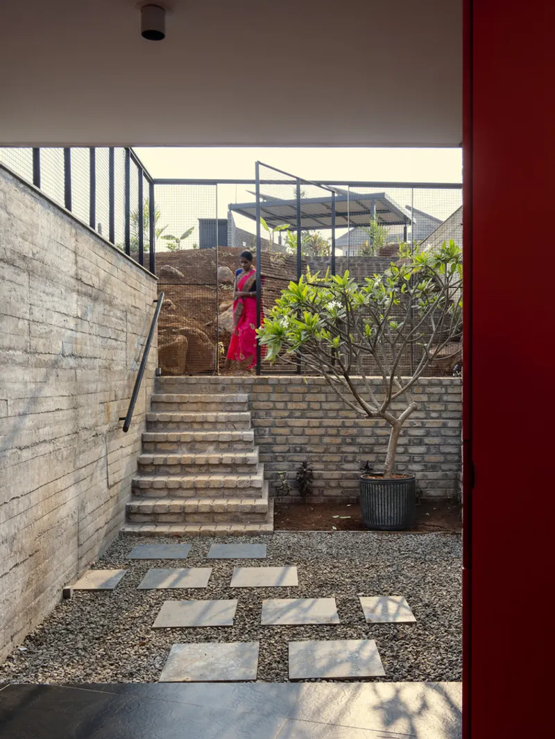 Exterior stair ascending through planted courtyard with brick walls and a figure in red