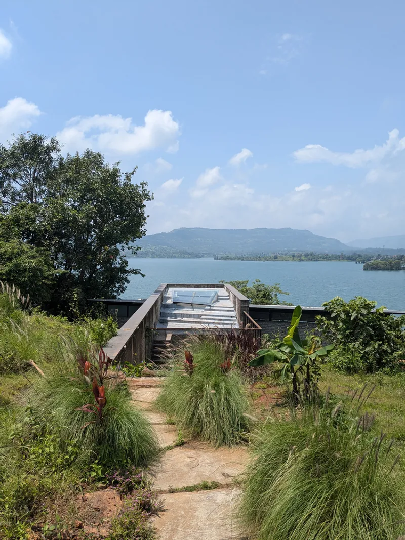 Path through planted grasses and banana palms leading to the angled roof terrace above the water
