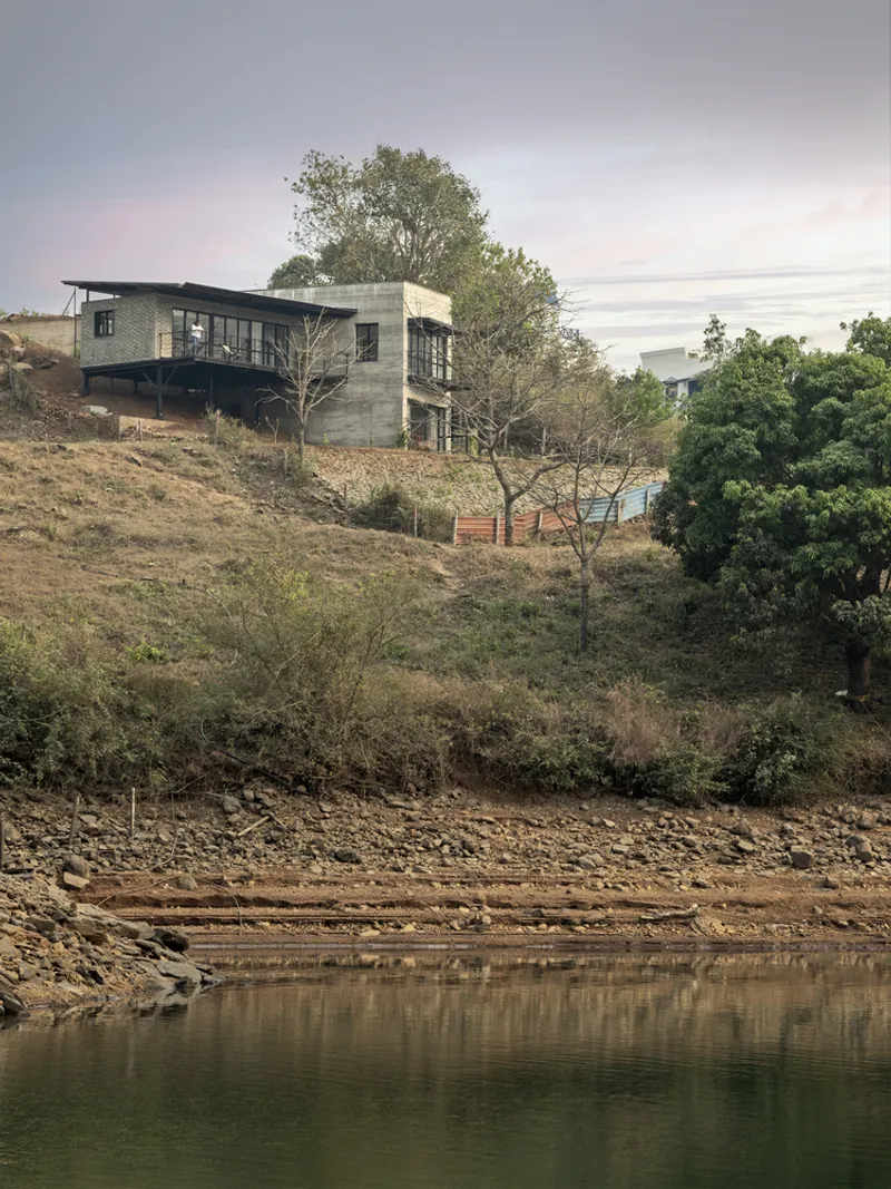 Two-storey residence perched on a sloping hillside above a still lake with scattered trees